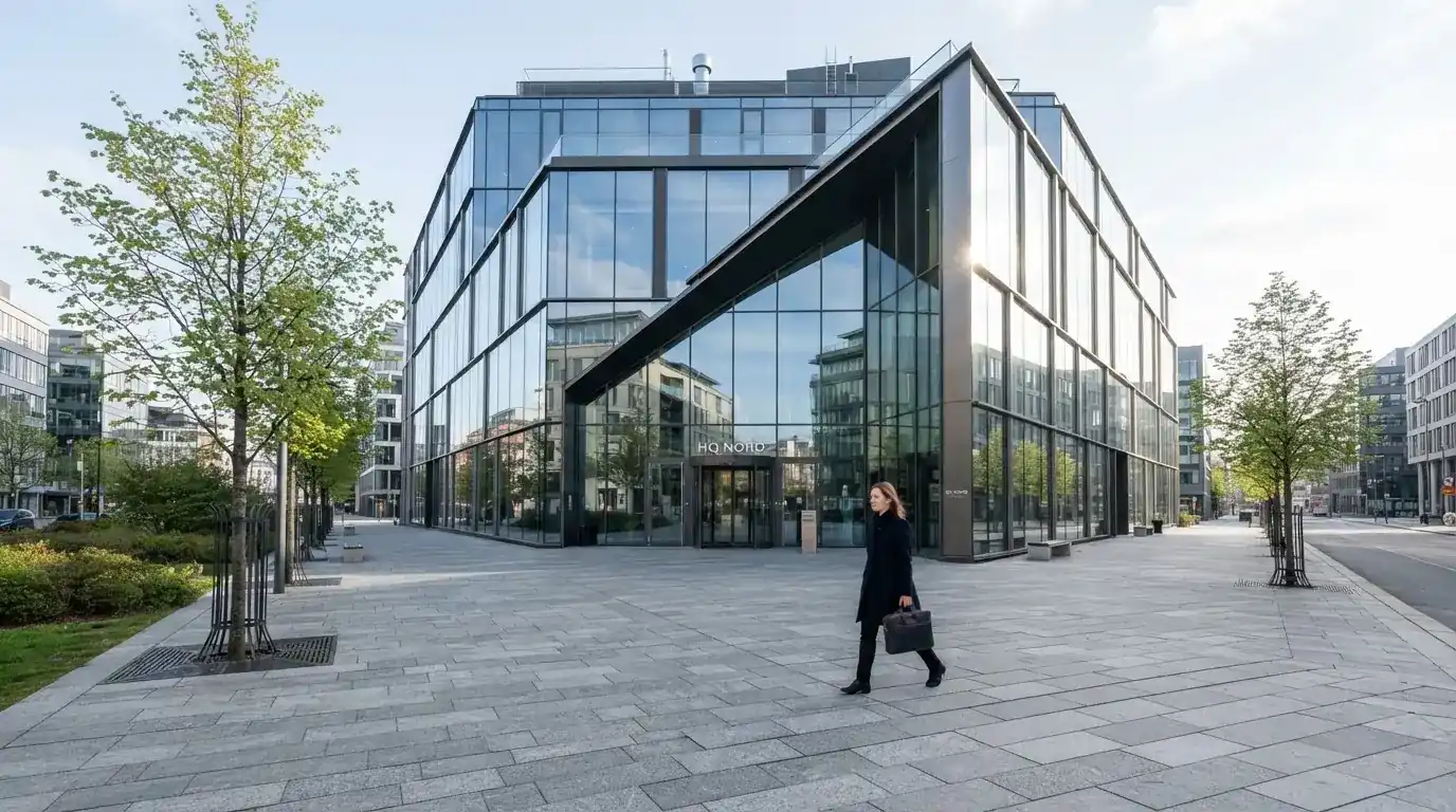 En moderne glasbygning i Ørestad en lys dag med en fodgænger i forgrunden og blå himmel bag facaden.